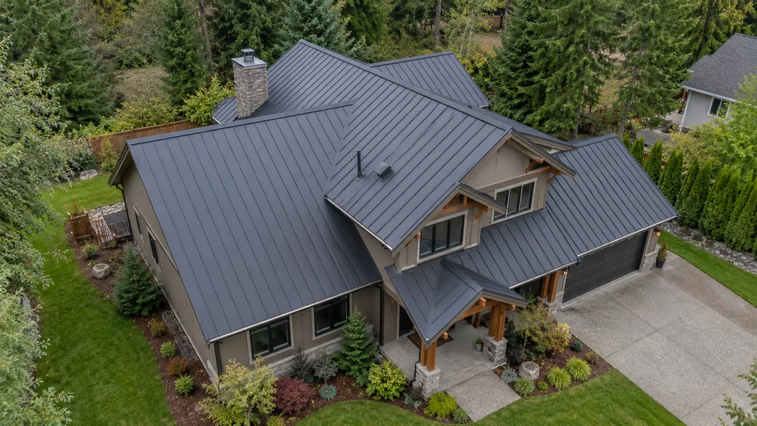 Oblique aerial view of a contemporary Pacific Northwest home with a standing-seam metal roof, framed by mature trees.